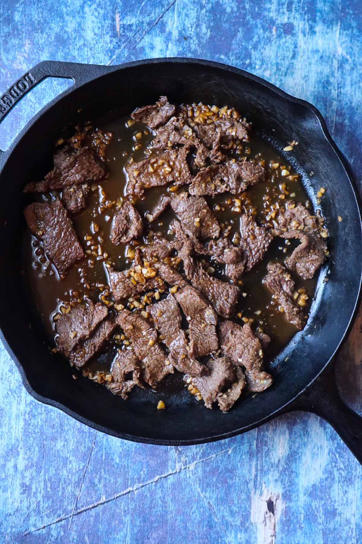 cast iron skillet with sliced steak cooked in a garlic stir fry sauce