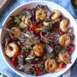 white plate with stir fry shrimp and steak topped with sesame seeds