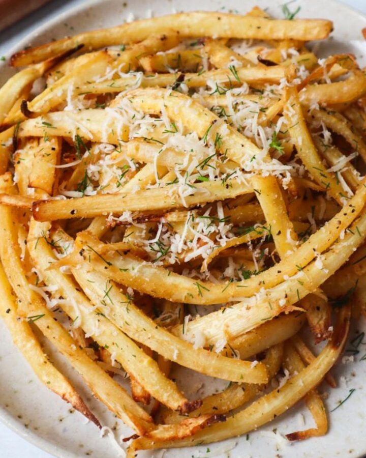 white plate with air fried parsnips topped with fresh herbs and cheese