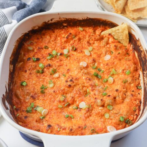 white baking dish with chip in the buffalo dip topped with green onion