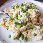plate with risotto topped with chicken, peas, and parsley