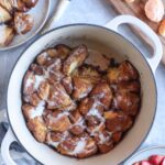 dutch oven with fully cooked monkey bread with a caramelized outer layer with cream cheese glaze over the top