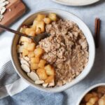 white bowl with oatmeal topped with cooked apples and sliced almonds