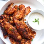 white bowl with blackened chicken tenders with a side of ranch topped with green onion.