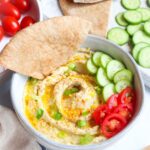 white bowl with lemon dill hummus with pita bread dipping into it.