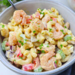 white bowl with macaroni salad tossed with old bay shrimp, red bell pepper, celery, topped with fresh parsley.