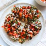 white plate with cooked chicken topped with bruschetta and balsamic glaze.