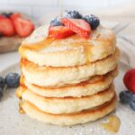 fluffy oat milk pancakes topped with strawberries, blueberries, and syrup.