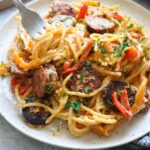 white plate with spoon scooping spaghetti topped with parsley.