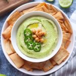 bowl with smooth jalapeno cilantro hummus surrounded by pita chips.