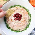 white bowl with kidney bean hummus with chip dipping into it.