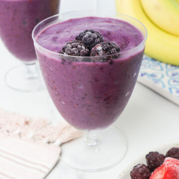 blackberry strawberry smoothie in a glass with frozen blackberries.