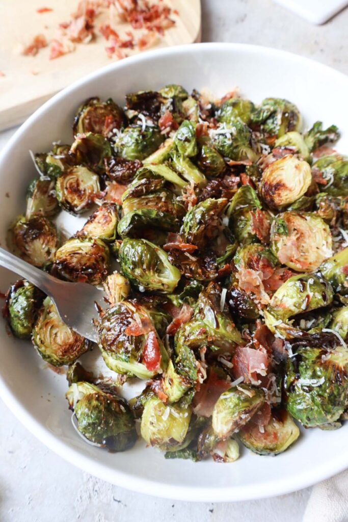 white bowl with brussels sprouts, parmesan cheese, prosciutto, and balsamic glaze.