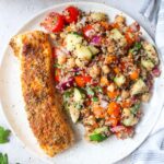 white plate with quinoa salad next to a seasoned salmon filet.