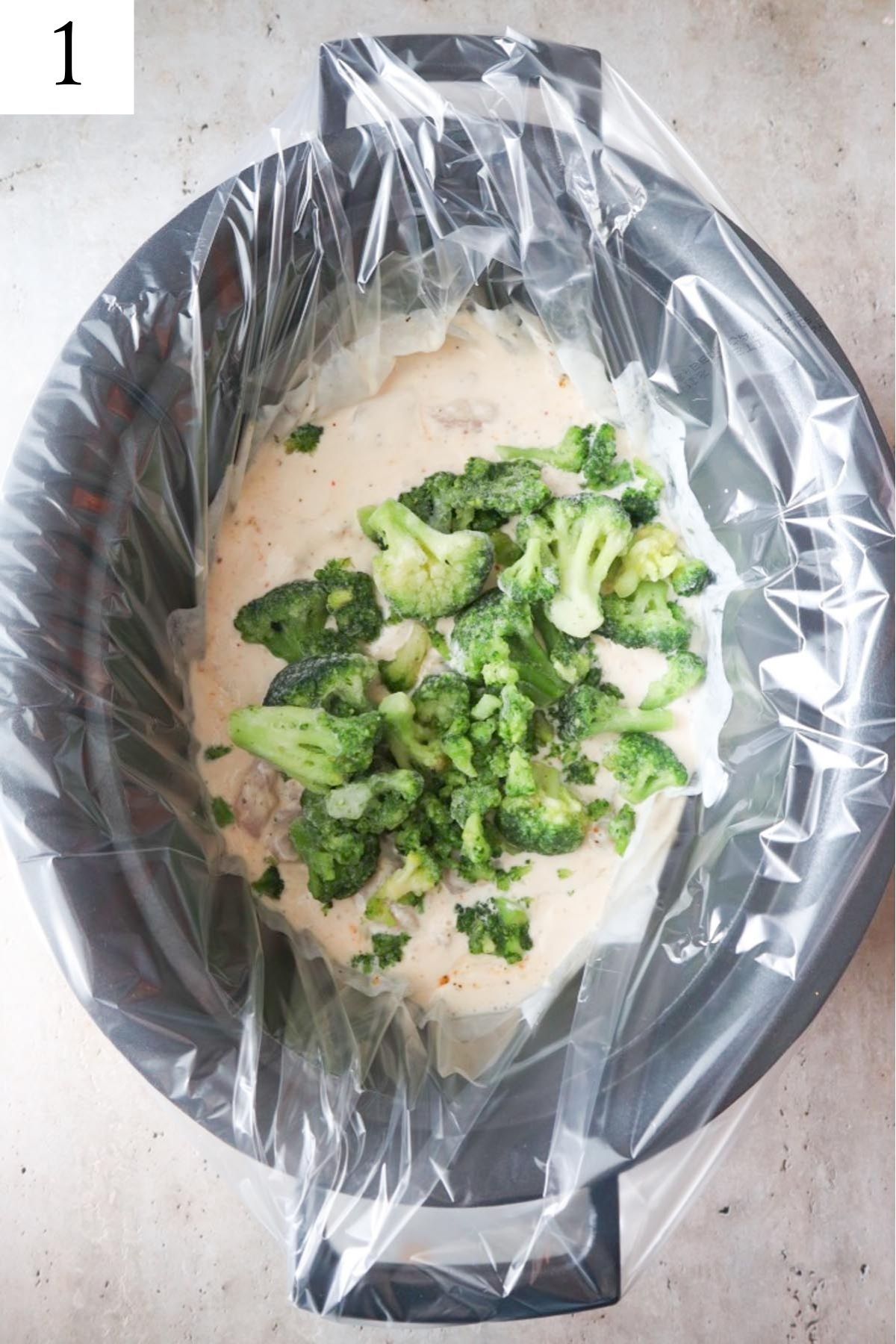 slow cooker with alfredo sauce topped with frozen broccoli.