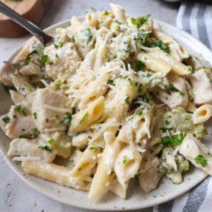 white plate with chicken alfredo with broccoli topped with fresh parsley and parmesan.