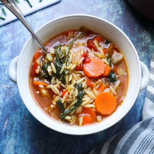 white bowl with vegetable orzo soup topped with fresh basil.