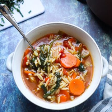 white bowl with vegetable orzo soup topped with fresh basil.