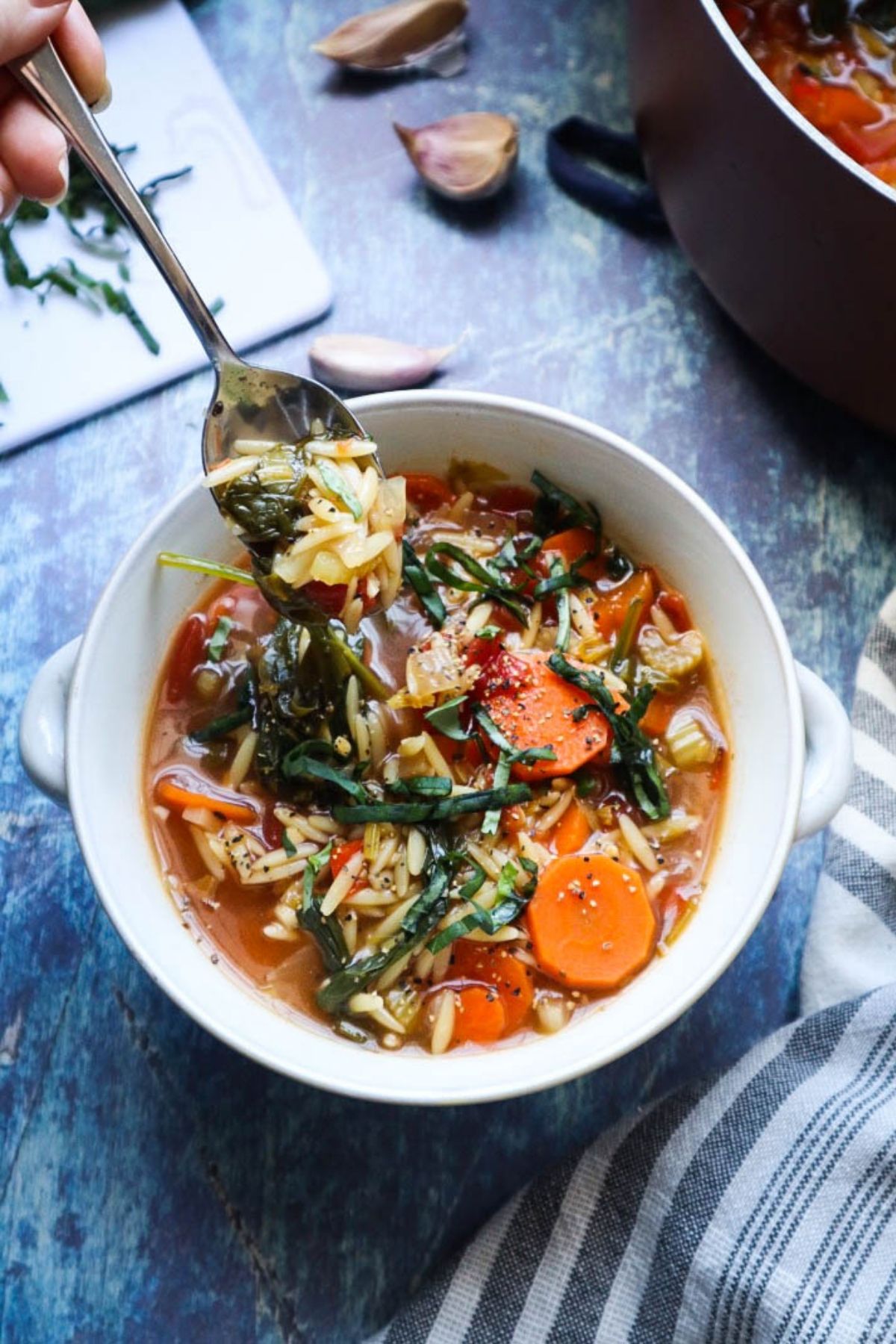 white glass bowl with orzo vegetable soup scooped up with a spoon.