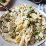 white plate with chicken alfredo with broccoli topped with fresh parsley and parmesan.
