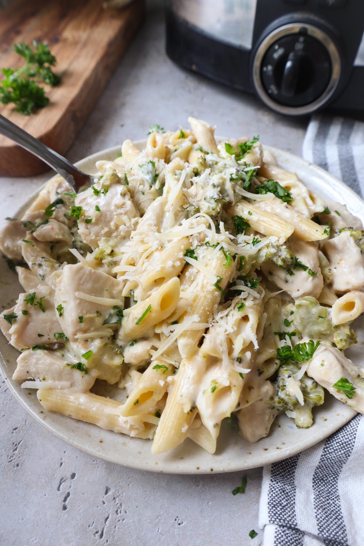 white plate with chicken alfredo with broccoli topped with fresh parsley and parmesan.