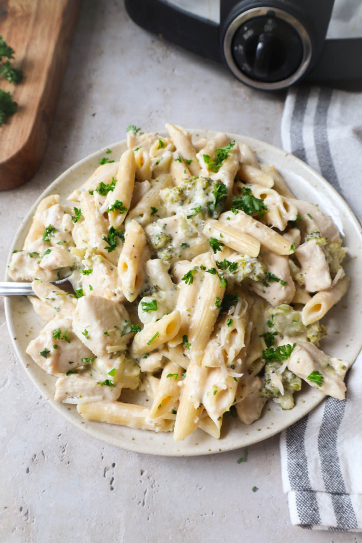 white plate with chicken alfredo with broccoli topped with fresh parsley and parmesan.