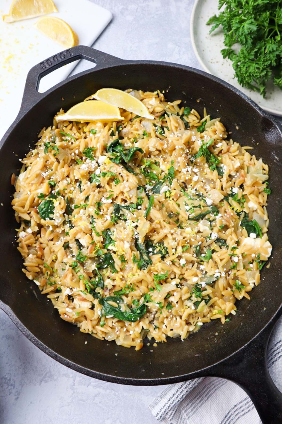skillet with lemon orzo topped with parsley and feta cheese.