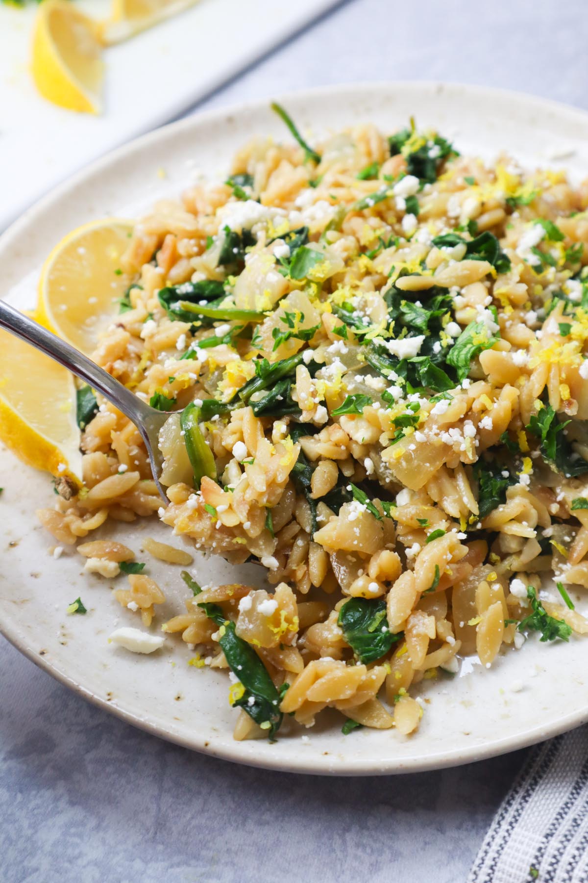 white plate with lemon spinach orzo topped with lemon zest and feta.