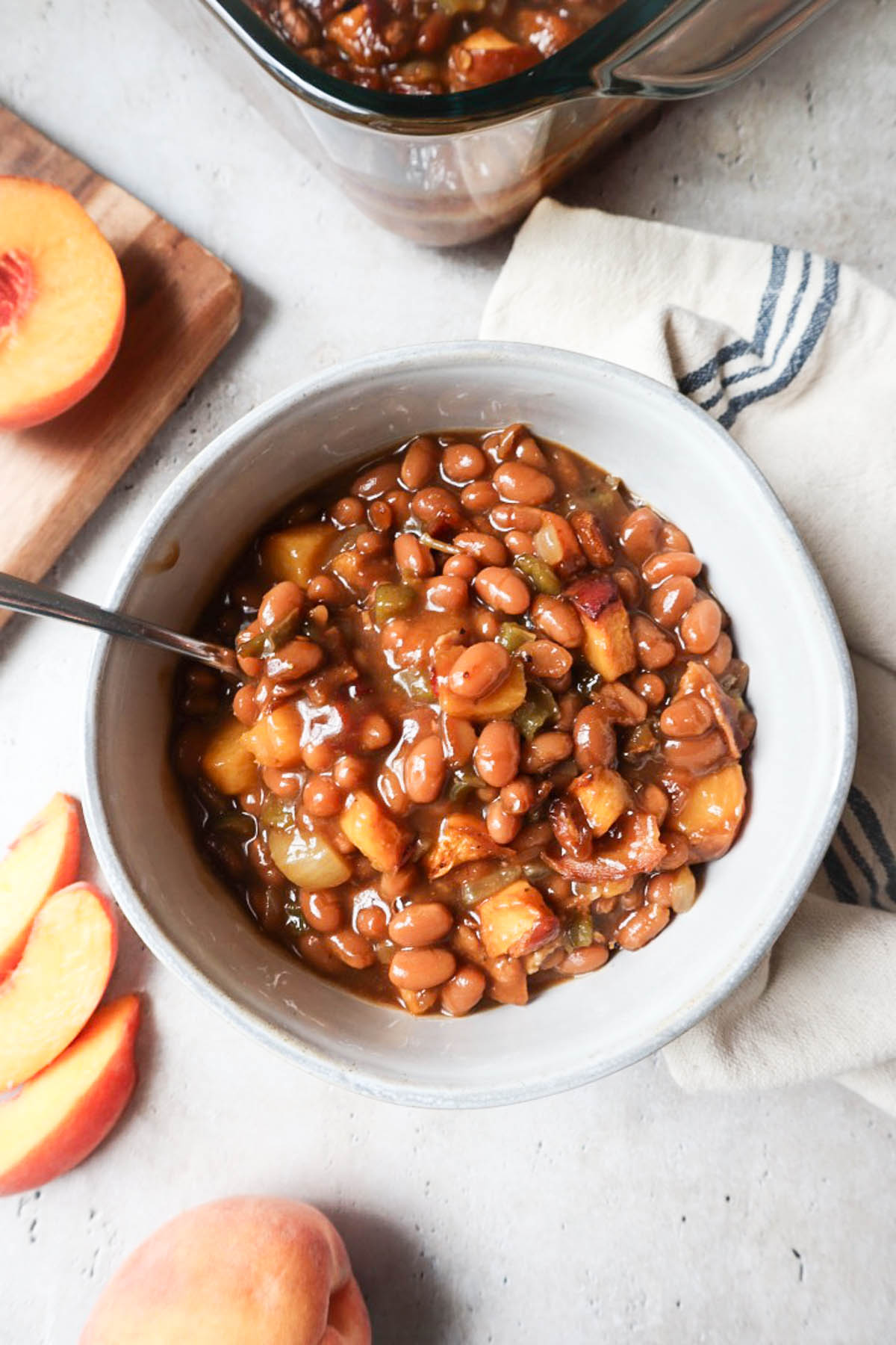 white bowl with peach baked beans surrounded by fresh peaches.