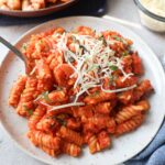 white plate with red pepper pasta with parmesan cheese and basil.