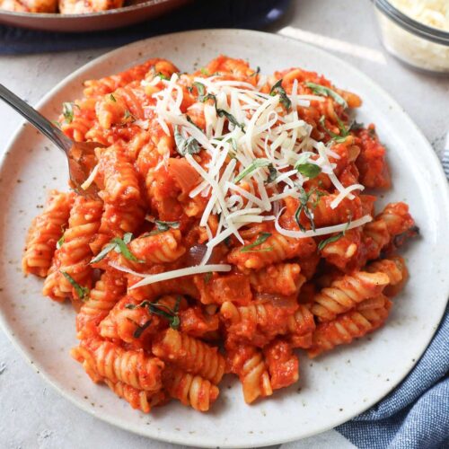 white plate with red pepper pasta with parmesan cheese and basil.