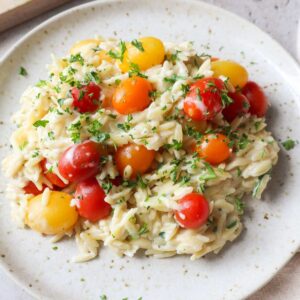 white plate with baked boursin orzo with tomatoes and parsley.