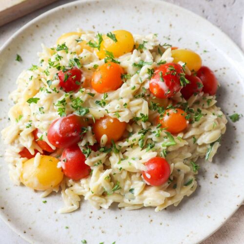 white plate with baked boursin orzo with tomatoes and parsley.