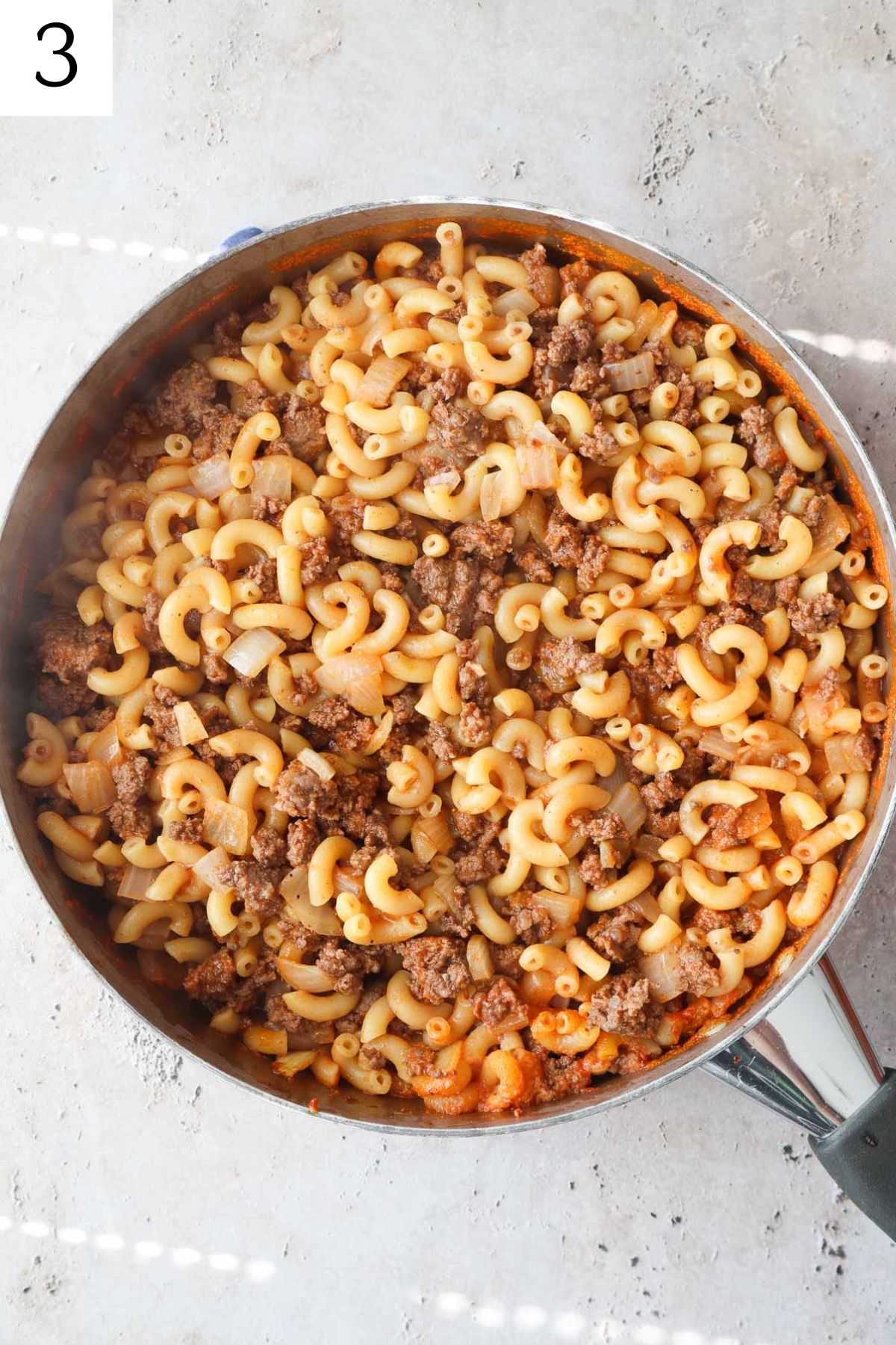 Skillet with cooked macaroni, ground beef, and onion.