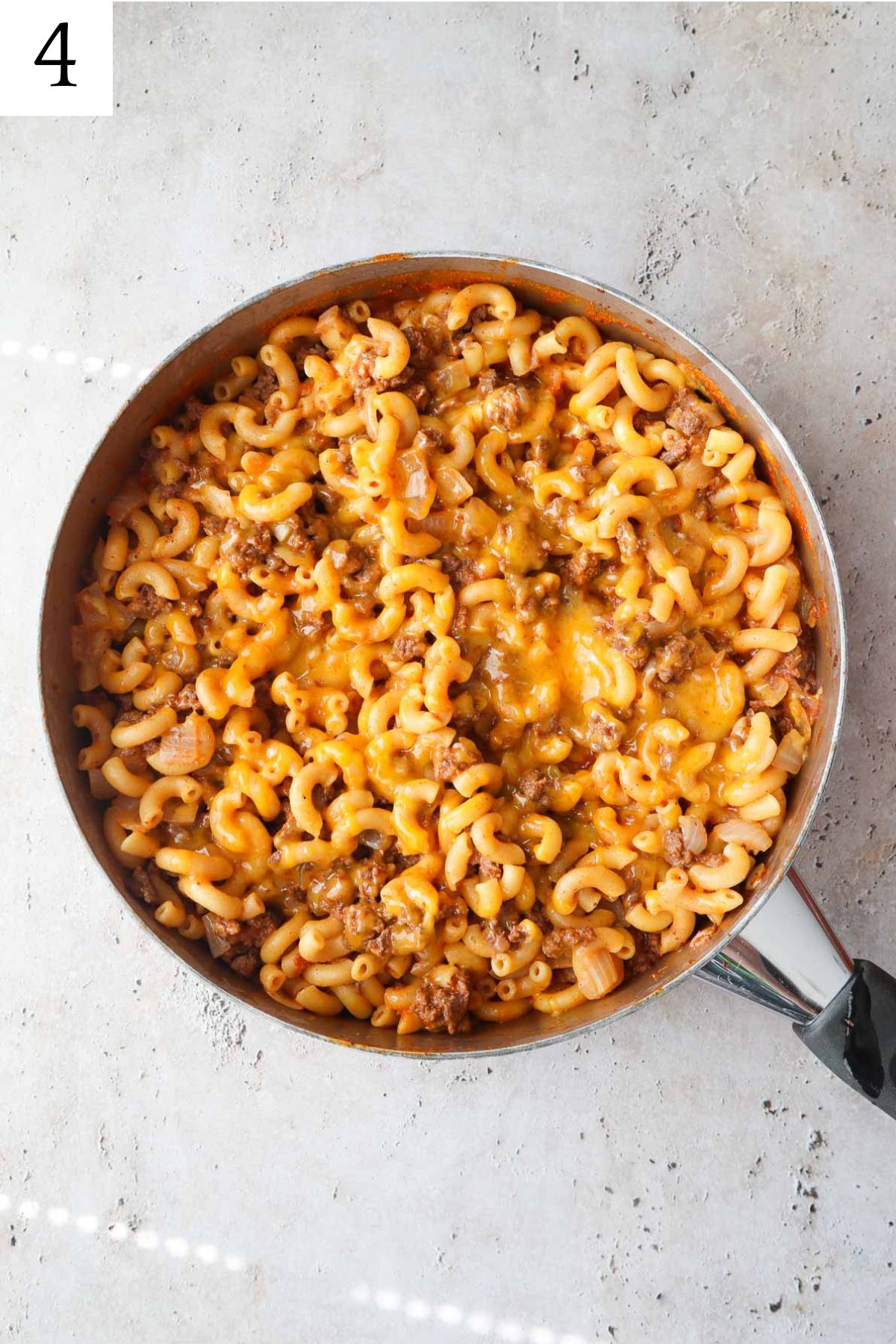 Skillet with cooked macaroni and ground beef topped with melted cheese.