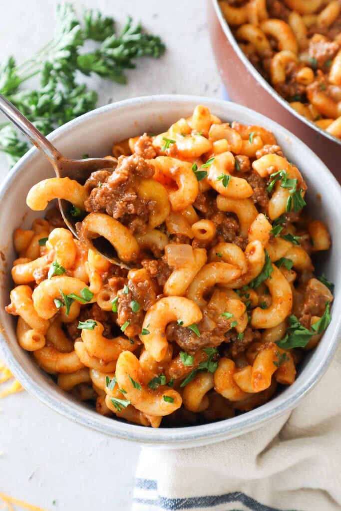 bowl with spoon scooping mac and cheese with ground beef.