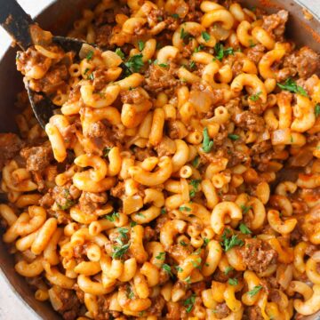 skillet with mac and cheese with ground beef topped with melted cheese and parsley.