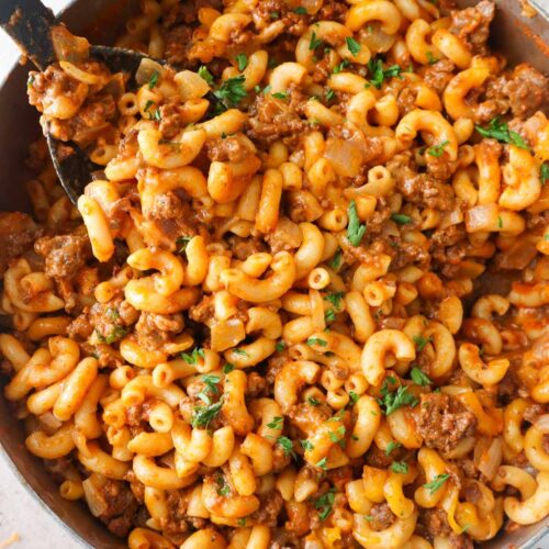 spoon scooping cheesy macaroni and ground beef topped with parsley.