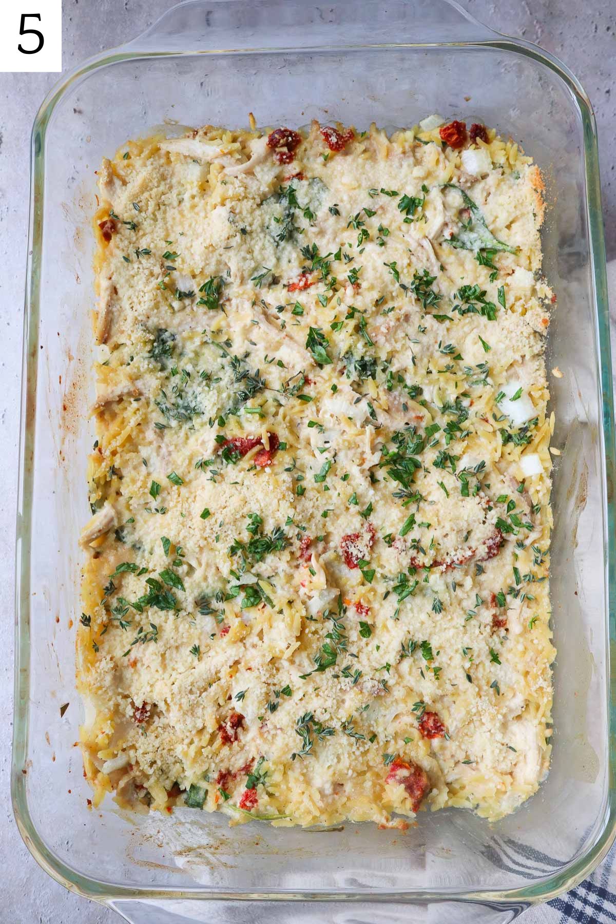 glass baking dish with creamy chicken orzo bake topped with parsley.
