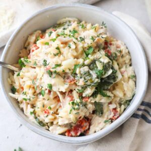 glass bowl with baked chicken orzo pasta topped with parsley.