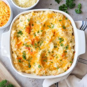 baked cheesy mashed potatoes with garlic in a baking dish topped with parsley.