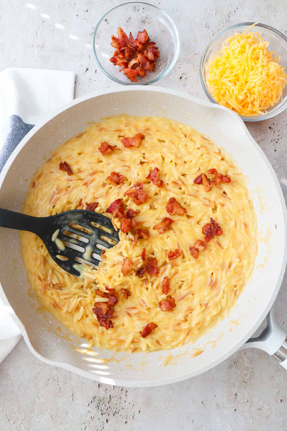 skillet with orzo mac and cheese topped with bacon.
