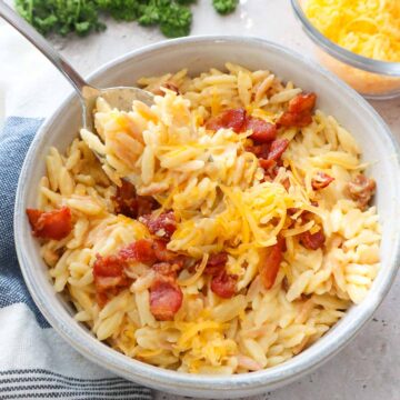 spoon scooping orzo mac and cheese topped with bacon and extra cheddar.