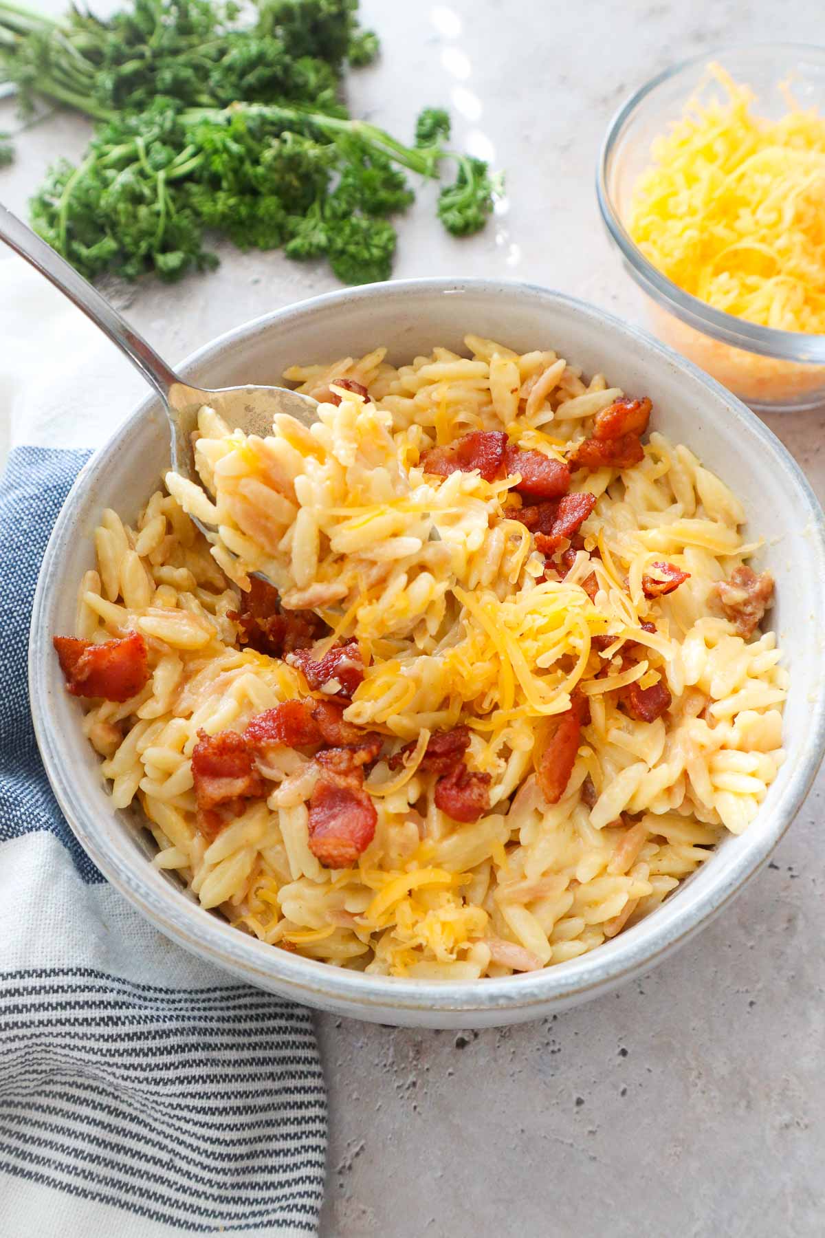 spoon scooping orzo mac and cheese topped with bacon and extra cheddar.