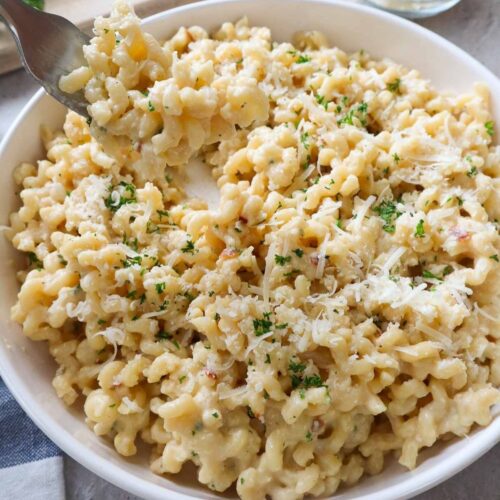 plate with roasted garlic pasta topped with parmesan and parsley.