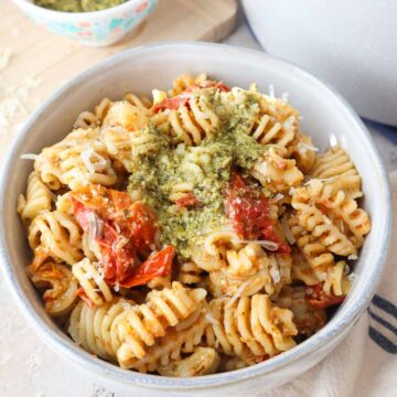 bowl with pesto pasta topped with cherry tomato sauce and more pesto.