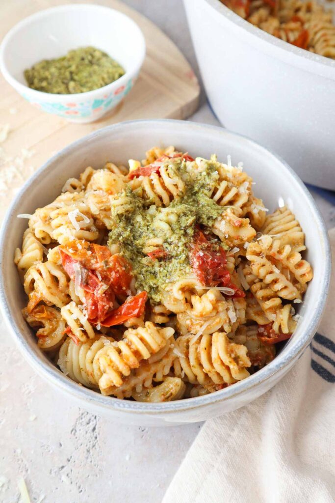 bowl with pesto pasta topped with cherry tomato sauce and more pesto.