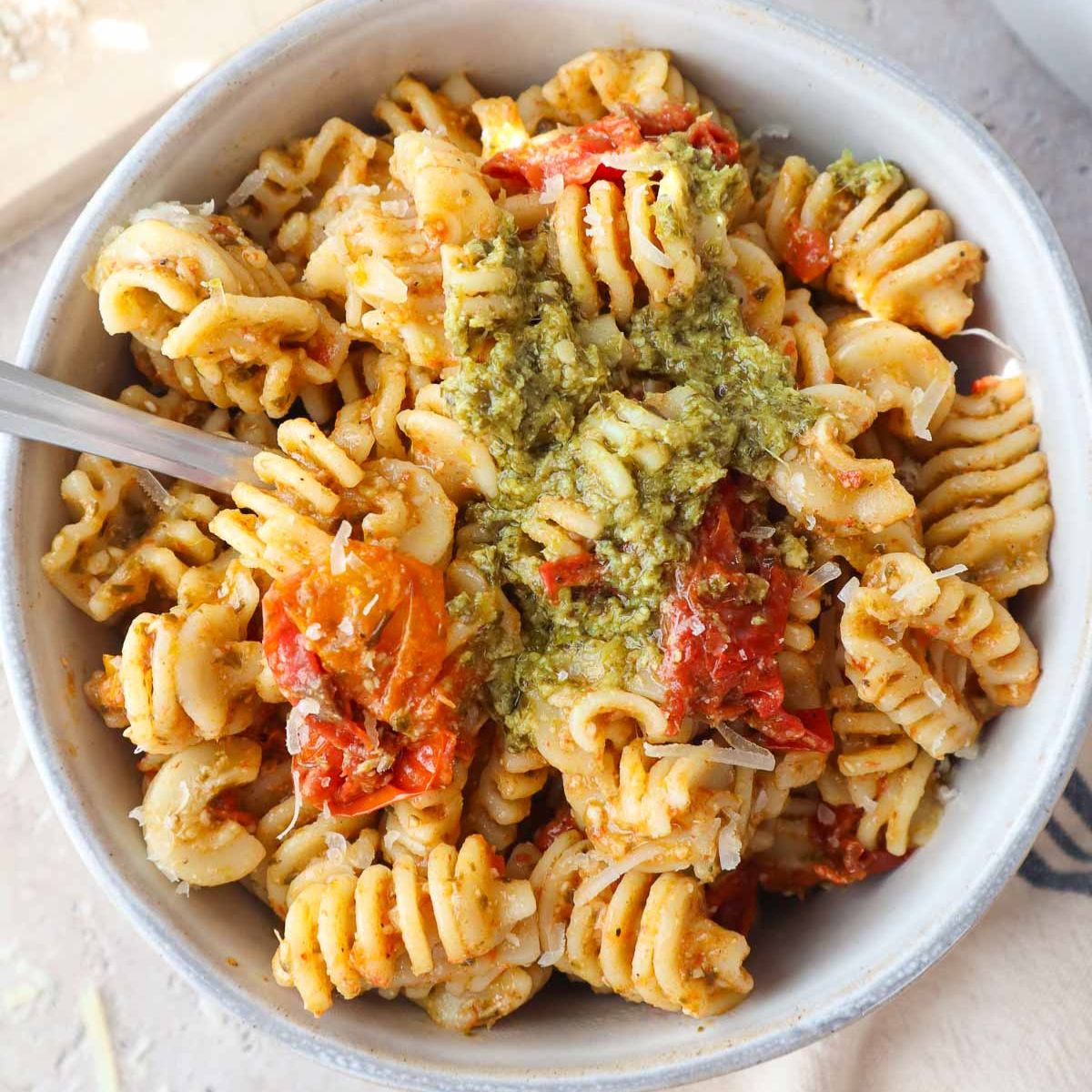 bowl with pesto pasta topped with cherry tomato sauce and more pesto.