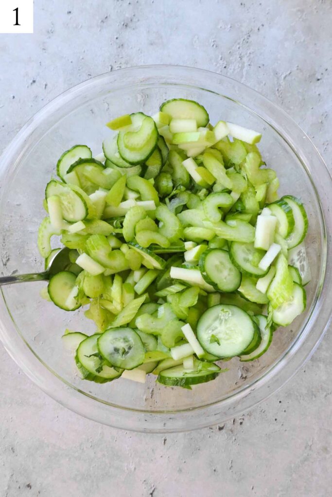 glass bowl with celery, cucumber, and apple tossed together.