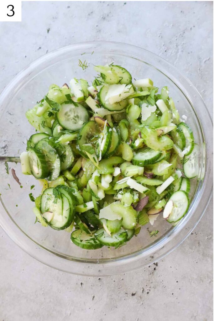 glass bowl with celery cucumber salad tossed in a dressing.